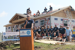 Man speaking at podium with new home construction and Farmers team members behind him