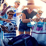 Woman in straw hat grabbing tote bag from car, next to a child in sunglasses holding a soccer ball